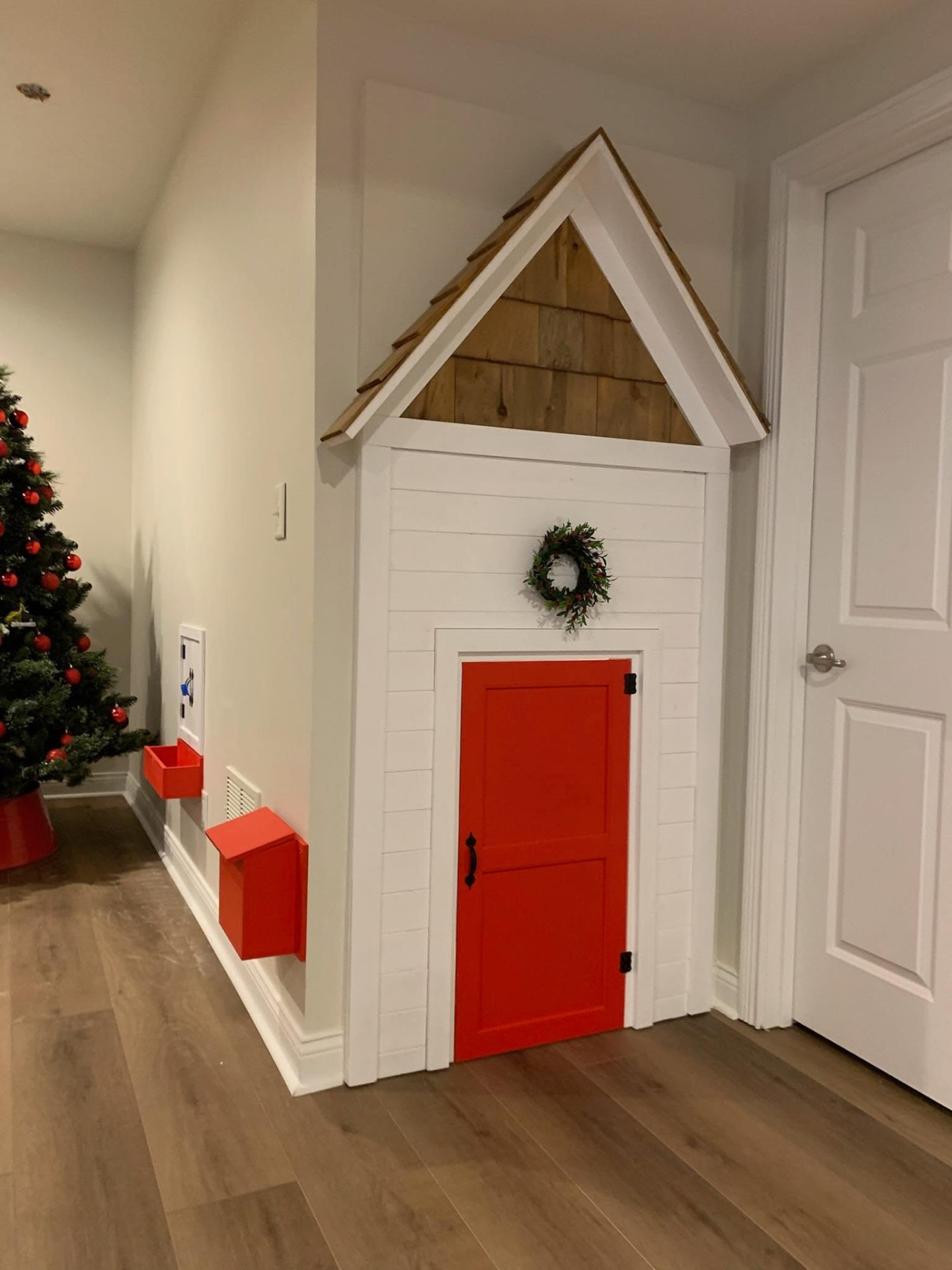 Under-stair playhouse with white shiplap siding, a bright red door, and a wood-shingled gable roof