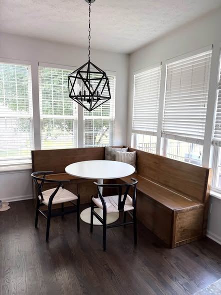 Dark stained wood corner banquette bench around a small round white table under a black pendant light