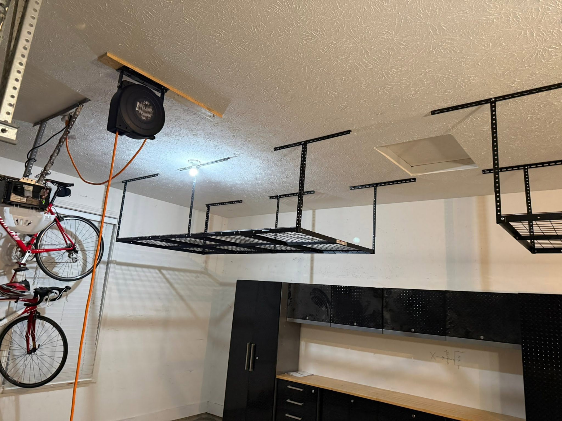 Black steel overhead storage racks mounted to a garage ceiling with bikes hanging on the wall