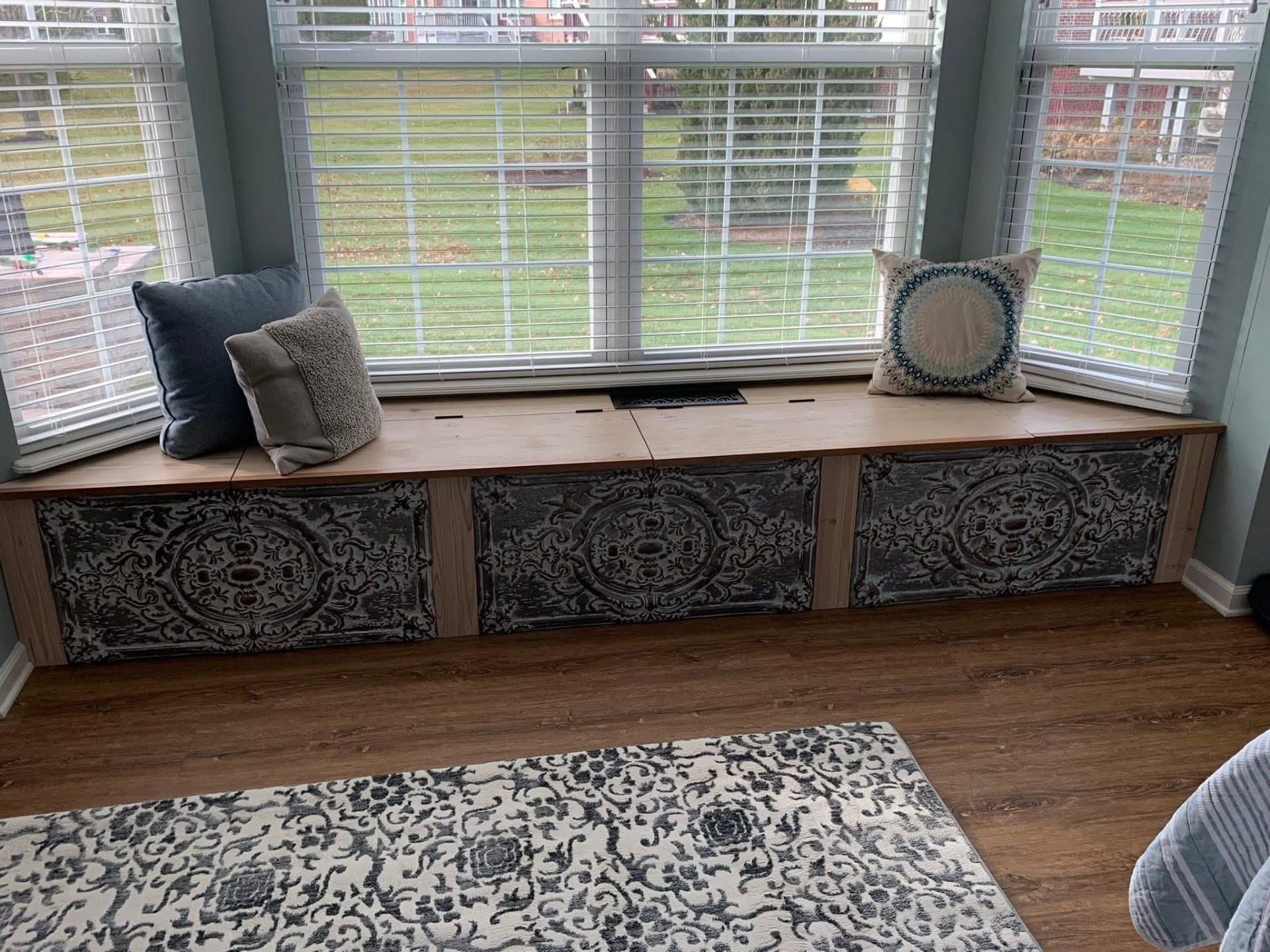 Built-in bay window bench seat with dark reclaimed pressed-tin panel fronts and painted wood trim
