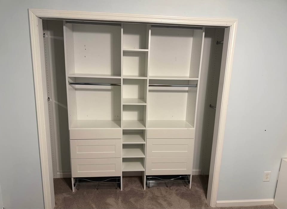 Newly installed white Dakota closet system with empty shelves, hanging rods, and drawers in a light blue bedroom
